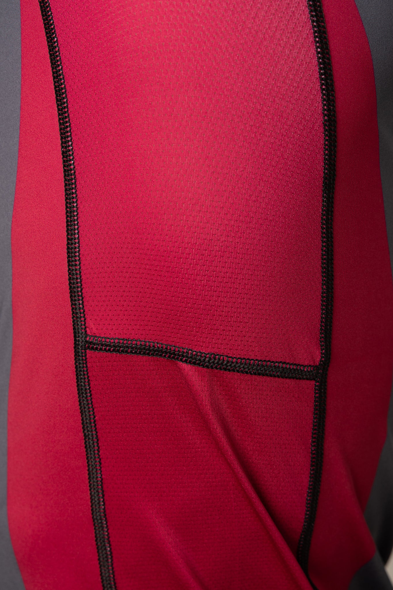 Detalle del panel granate y las costuras reforzadas de la rashguard gris