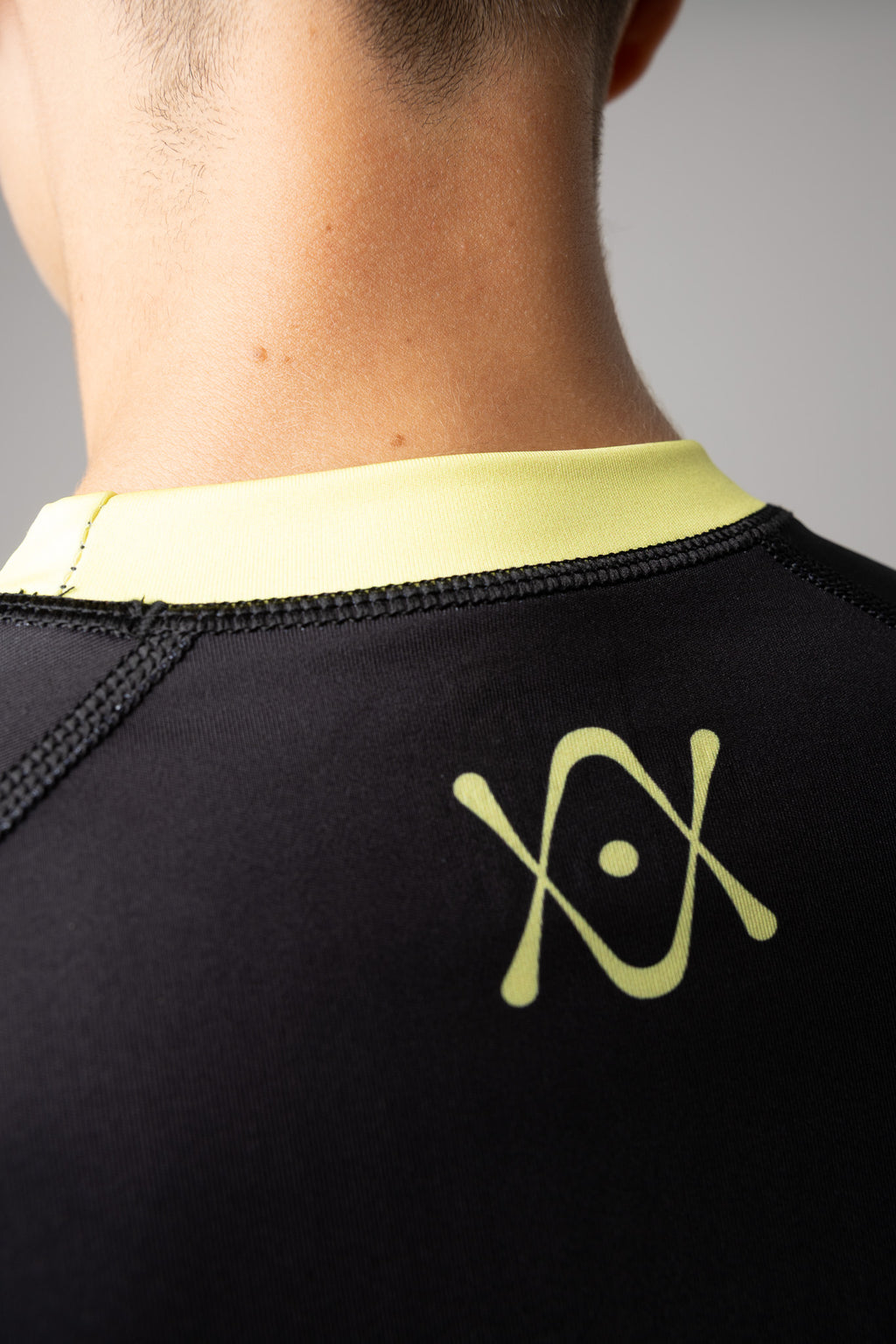 Detalle del logo AUTŌRITA en la espalda de una rashguard negra y amarilla para BJJ.