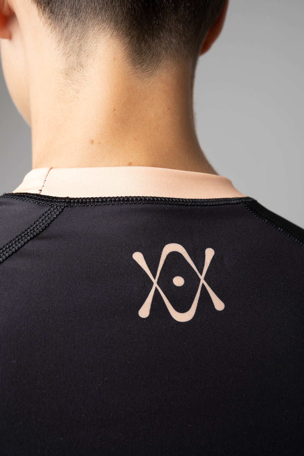 Detalle del logo AUTŌRITA en la espalda de una rashguard negra y naranja para BJJ.