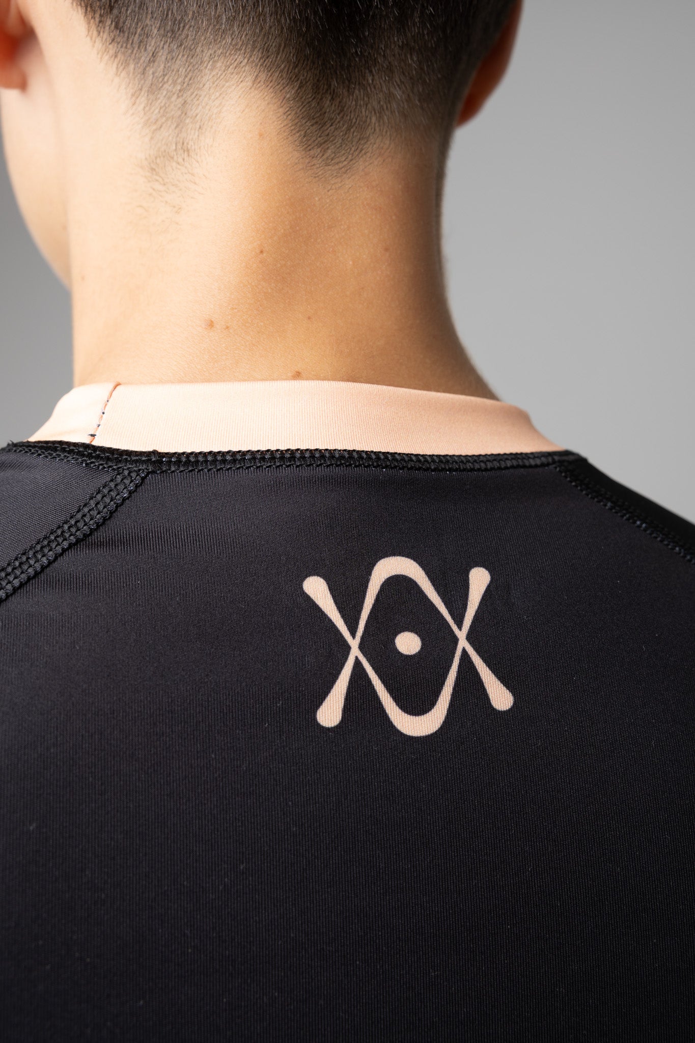 Detalle del logo AUTŌRITA en la espalda de una rashguard negra y naranja para BJJ.