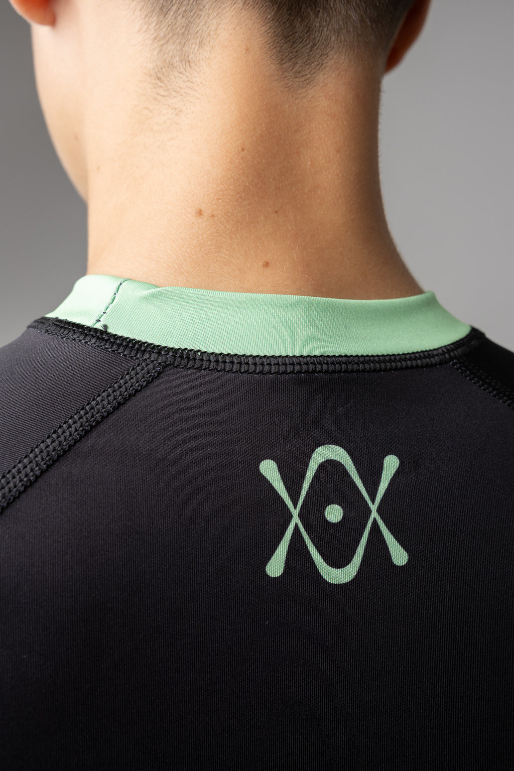 Detalle del logo AUTŌRITA en la espalda de una rashguard negra y verde para BJJ.