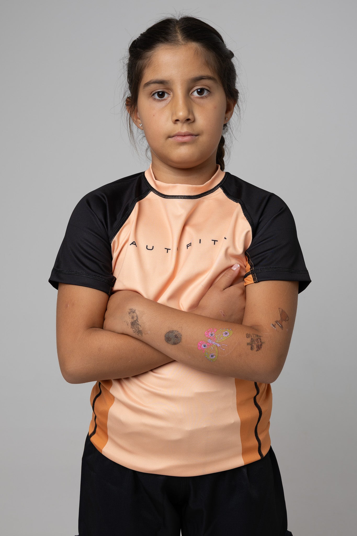 Licra naranja AUTŌRITA kids para grappling con ajuste deportivo y modelo en brazos cruzados.