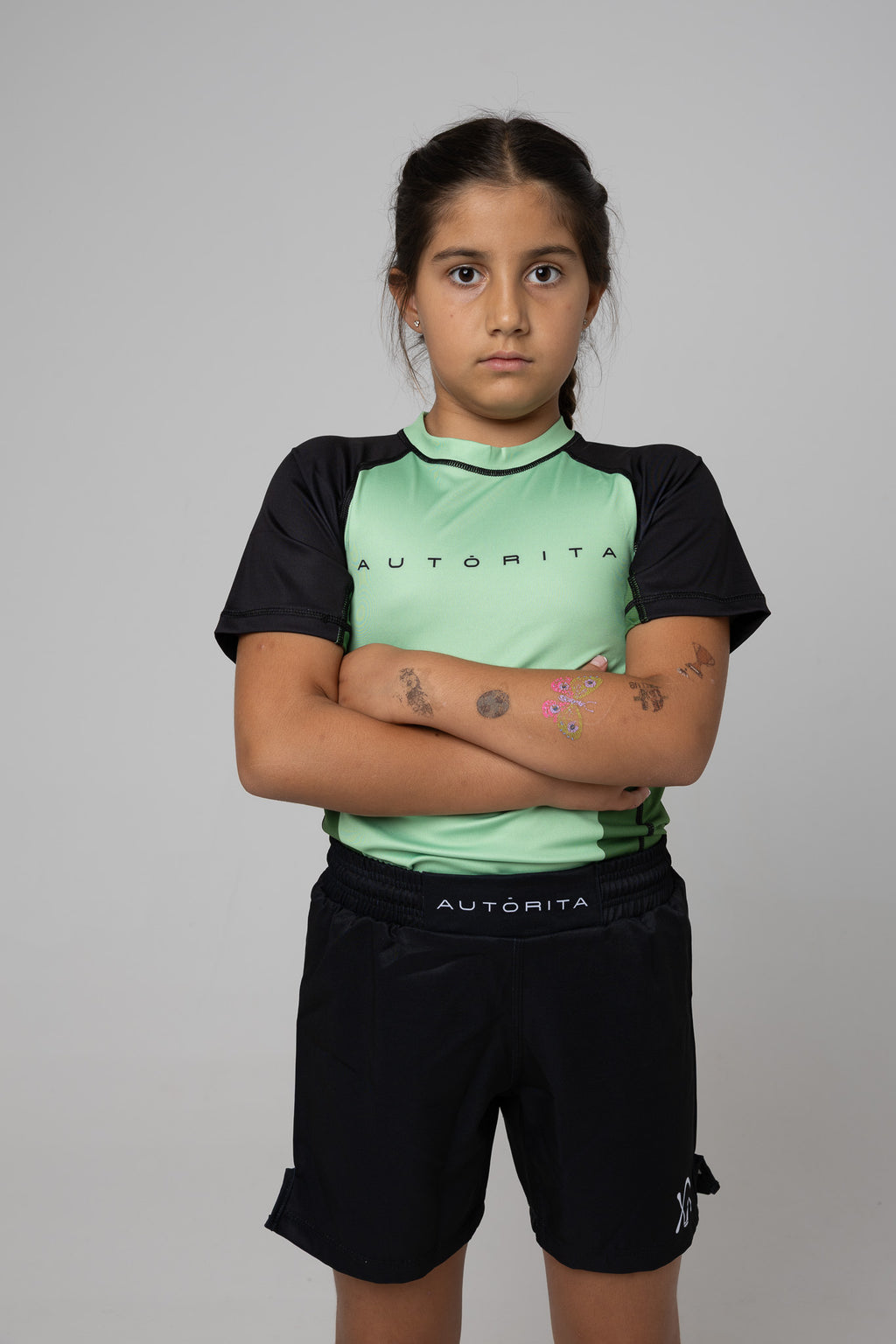 Licra verde AUTŌRITA kids para grappling con modelo en brazos cruzados y estética deportiva.