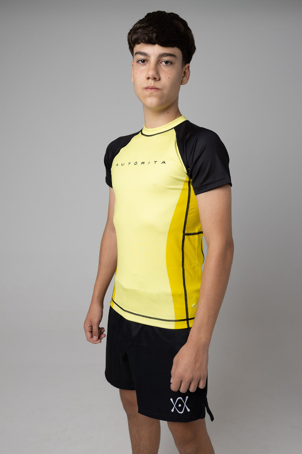 Vista lateral de rashguard amarilla AUTŌRITA juvenil con mangas negras para entrenamiento de BJJ.