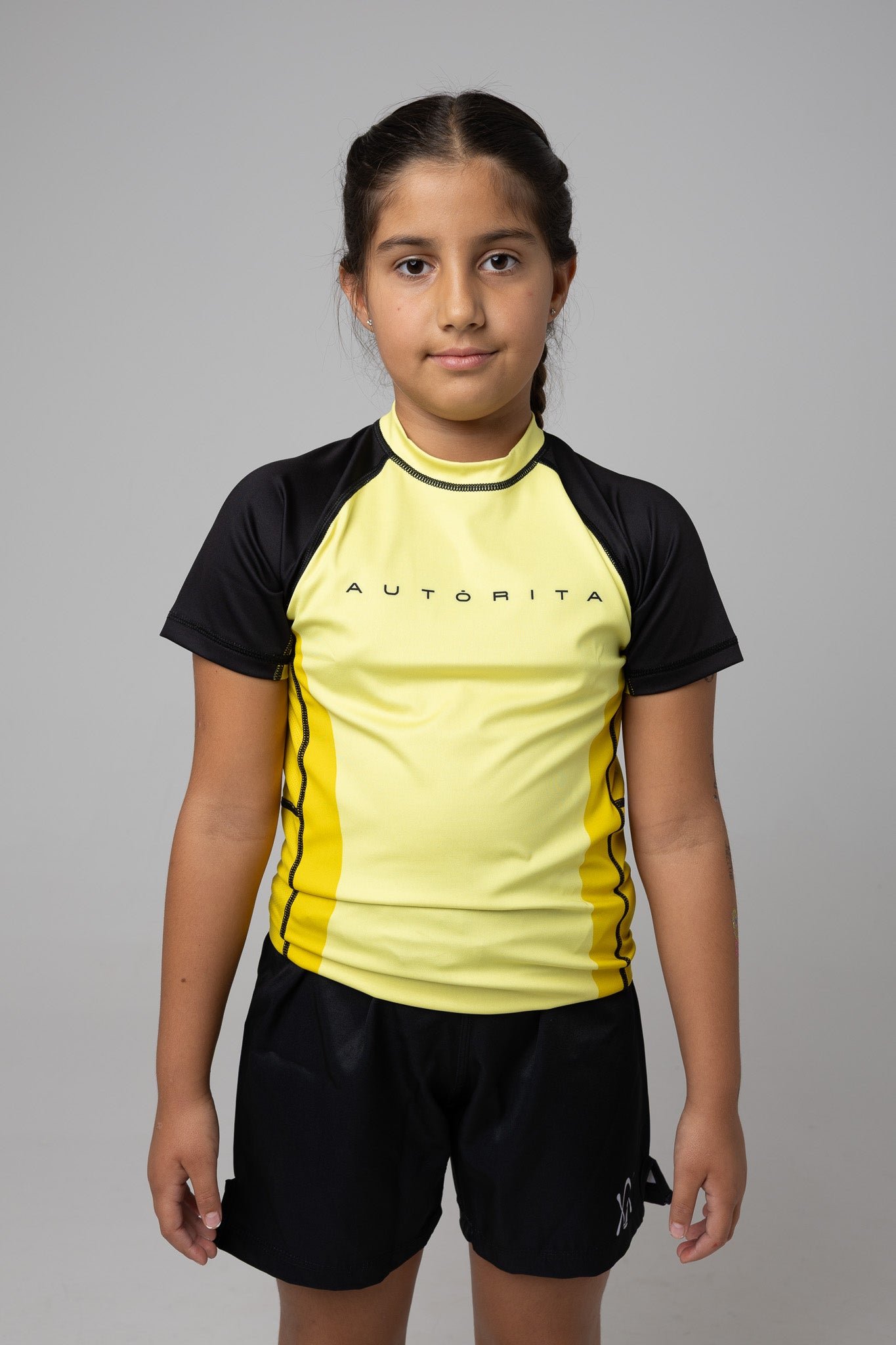 Vista frontal de rashguard amarilla y negra AUTŌRITA kids para Brazilian Jiu-Jitsu.