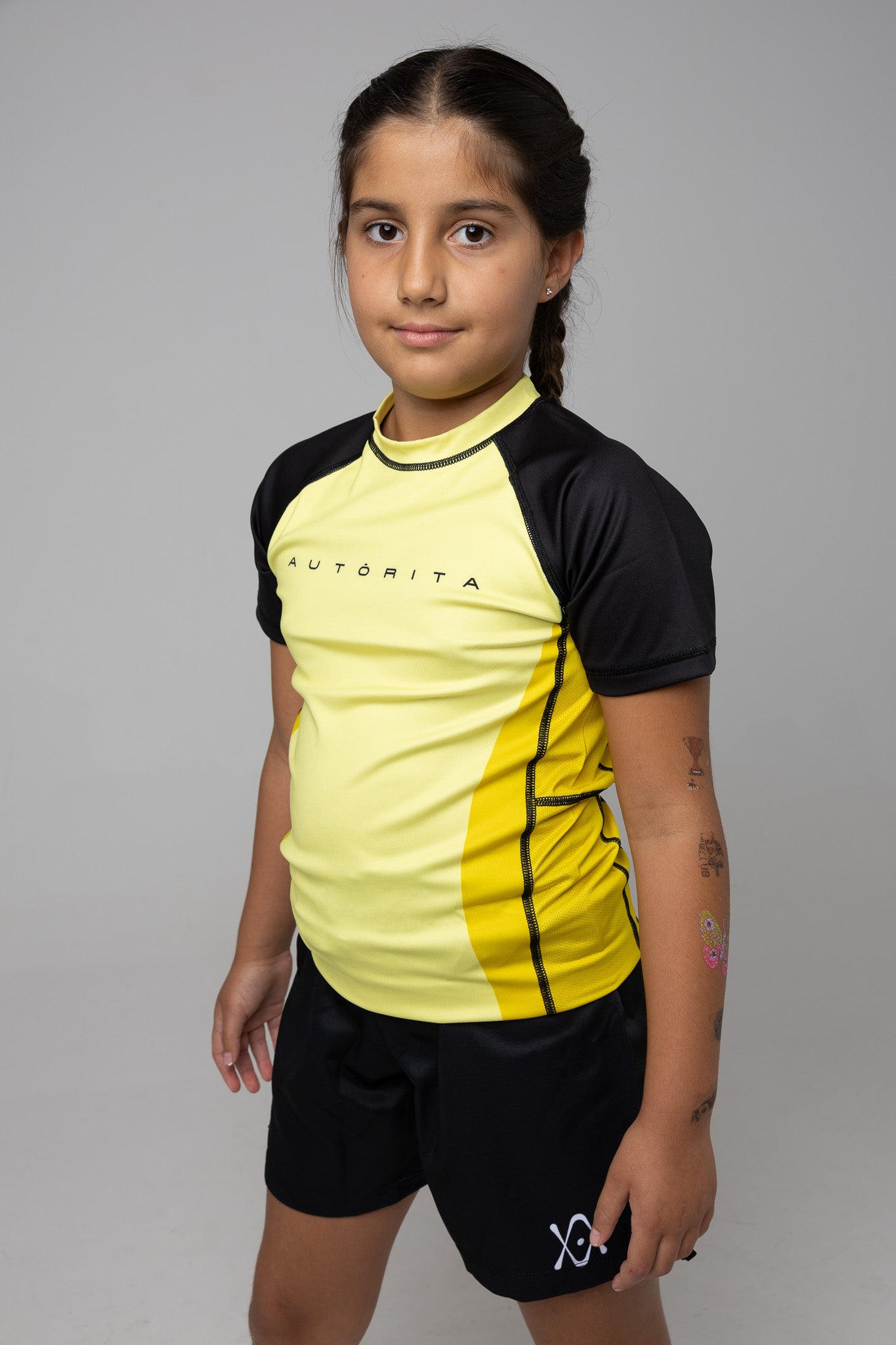 Modelo infantil con rashguard amarilla y negra AUTŌRITA para Brazilian Jiu-Jitsu en estudio.