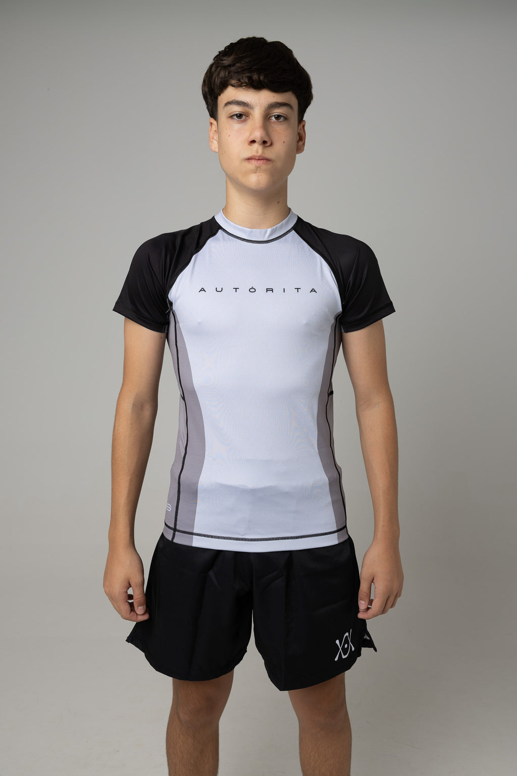 Vista frontal de rashguard juvenil gris y negra AUTŌRITA para Brazilian Jiu-Jitsu.