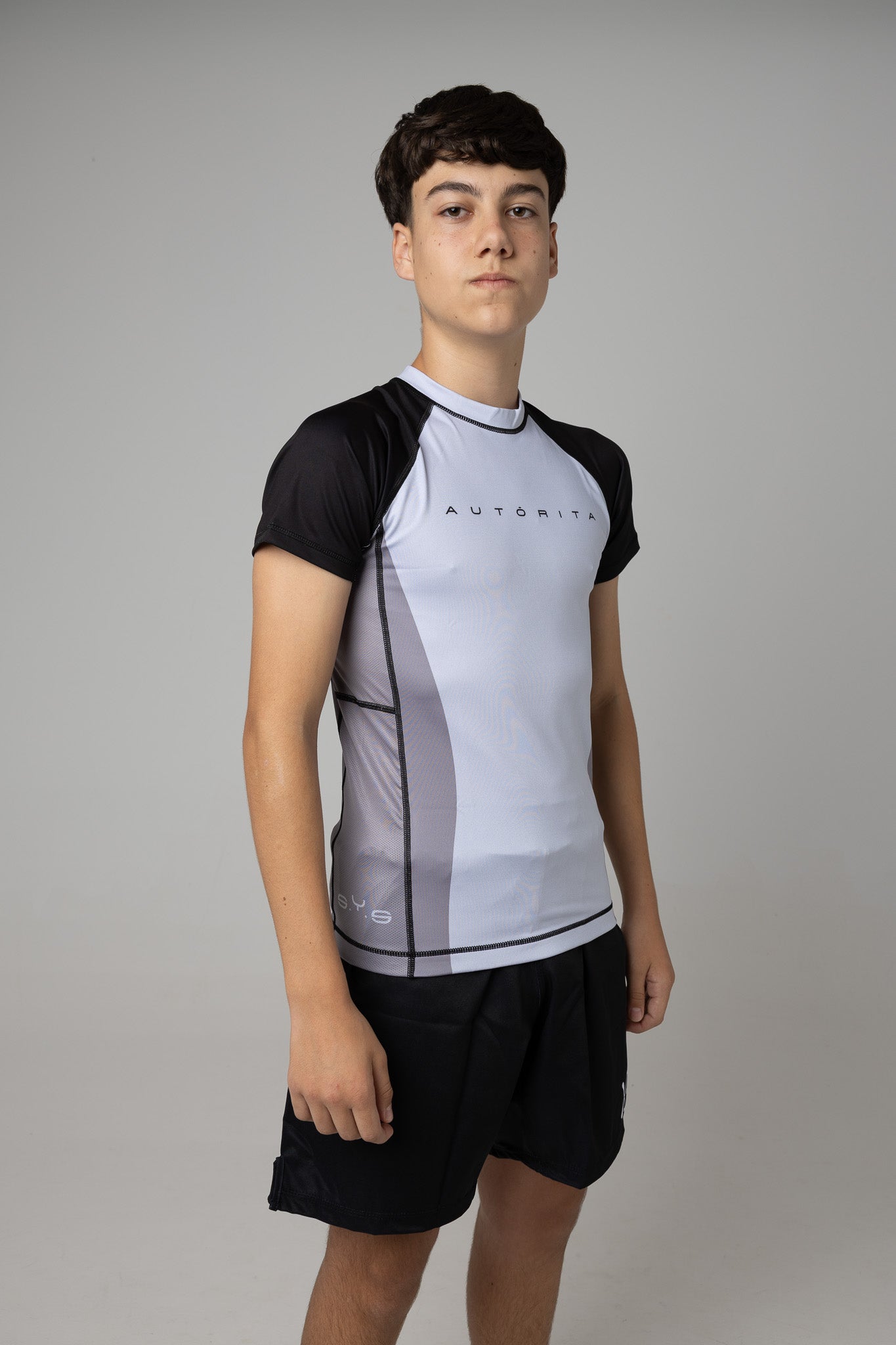 Vista lateral de rashguard gris y negra AUTŌRITA juvenil para BJJ y entrenamiento.