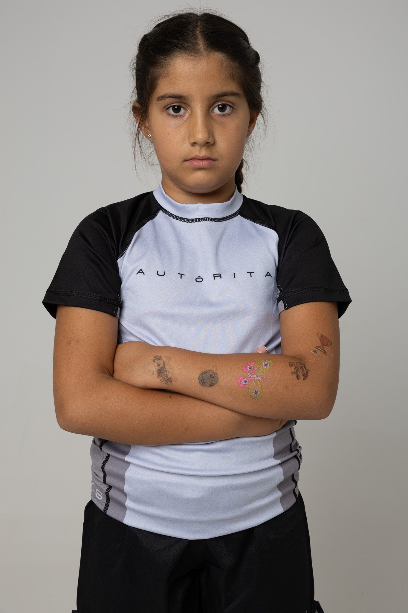 Modelo infantil con rashguard gris y negra AUTŌRITA para BJJ, brazos cruzados