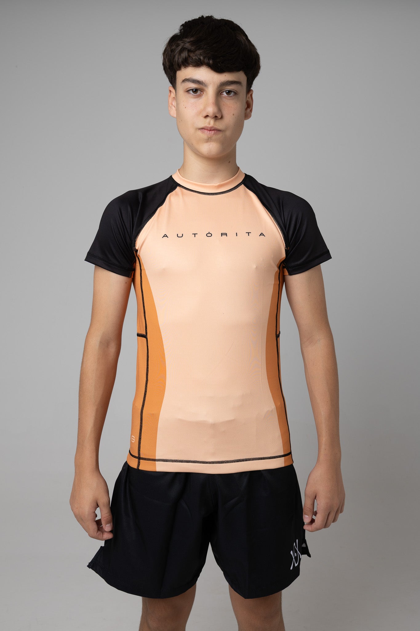 Vista frontal de rashguard naranja AUTŌRITA juvenil para Brazilian Jiu-Jitsu y entrenamiento de grappling.