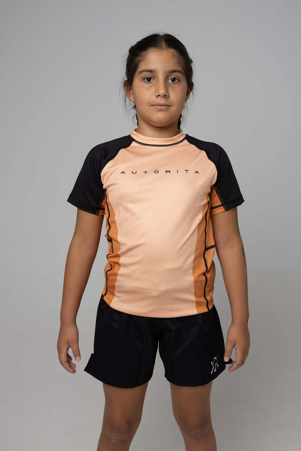 Vista frontal de rashguard naranja AUTŌRITA kids para Brazilian Jiu-Jitsu, grappling y entrenamiento.
