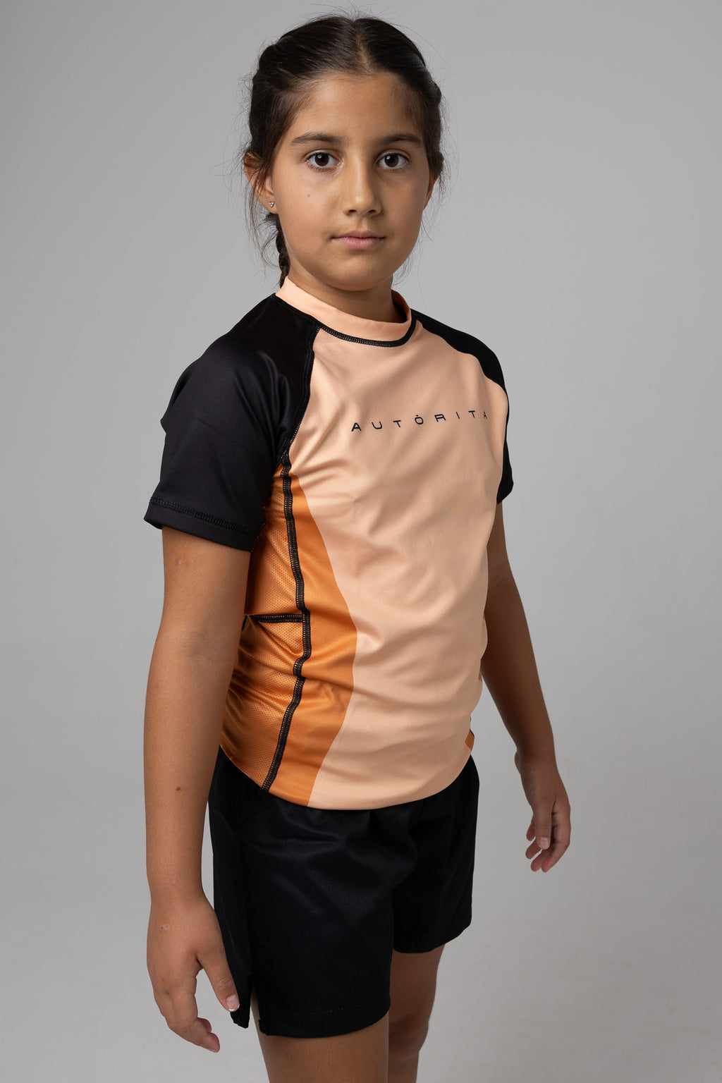 Rashguard naranja AUTŌRITA kids para Brazilian Jiu-Jitsu y grappling, vista lateral con panel técnico.