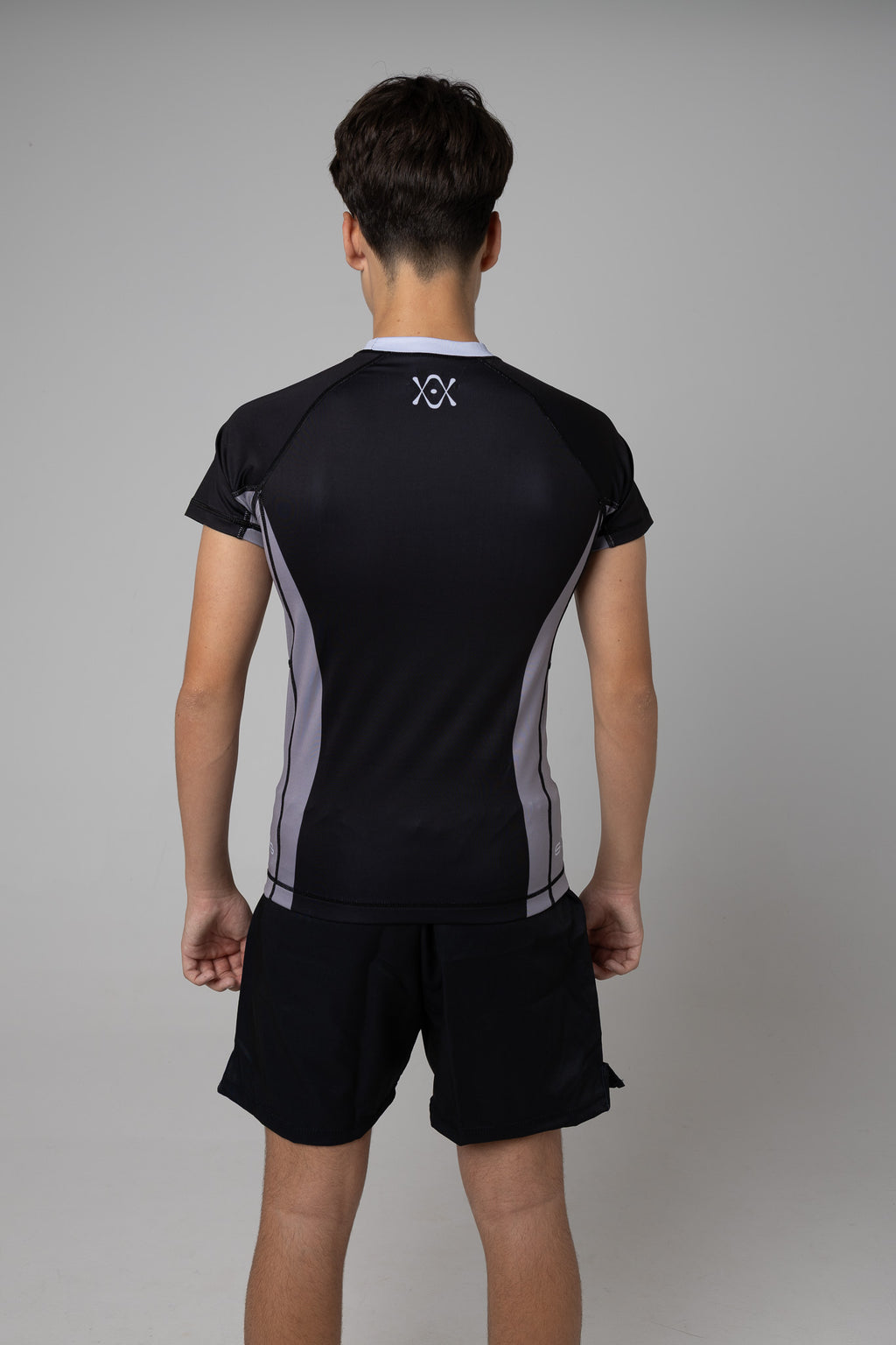 Vista trasera de rashguard negra y gris AUTŌRITA juvenil con logo superior en la espalda.