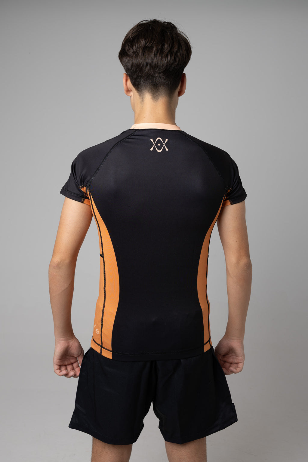 Vista trasera de rashguard negra y naranja AUTŌRITA juvenil para BJJ con logo superior en la espalda.