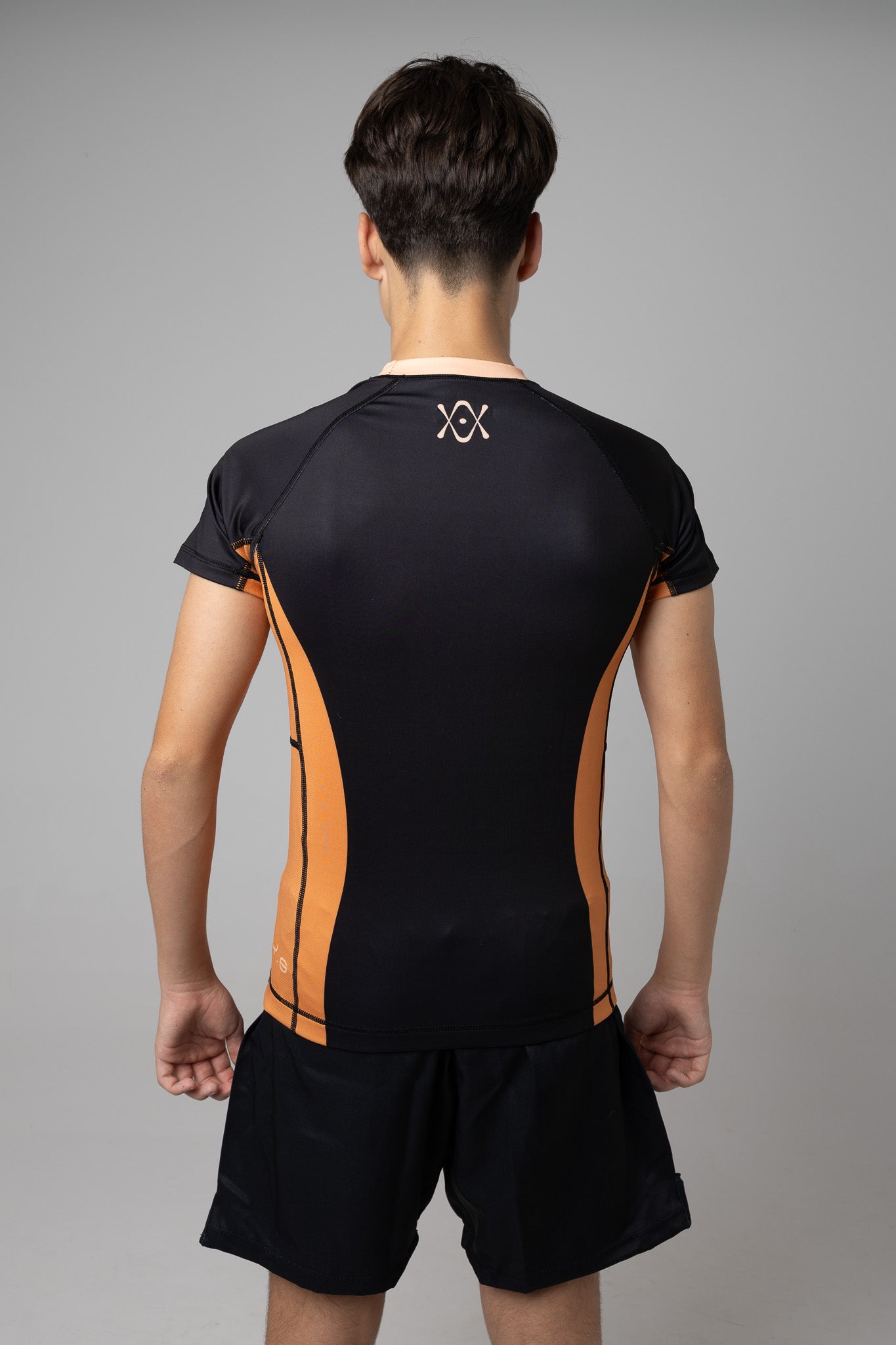 Vista trasera de rashguard negra y naranja AUTŌRITA juvenil para BJJ con logo superior en la espalda.