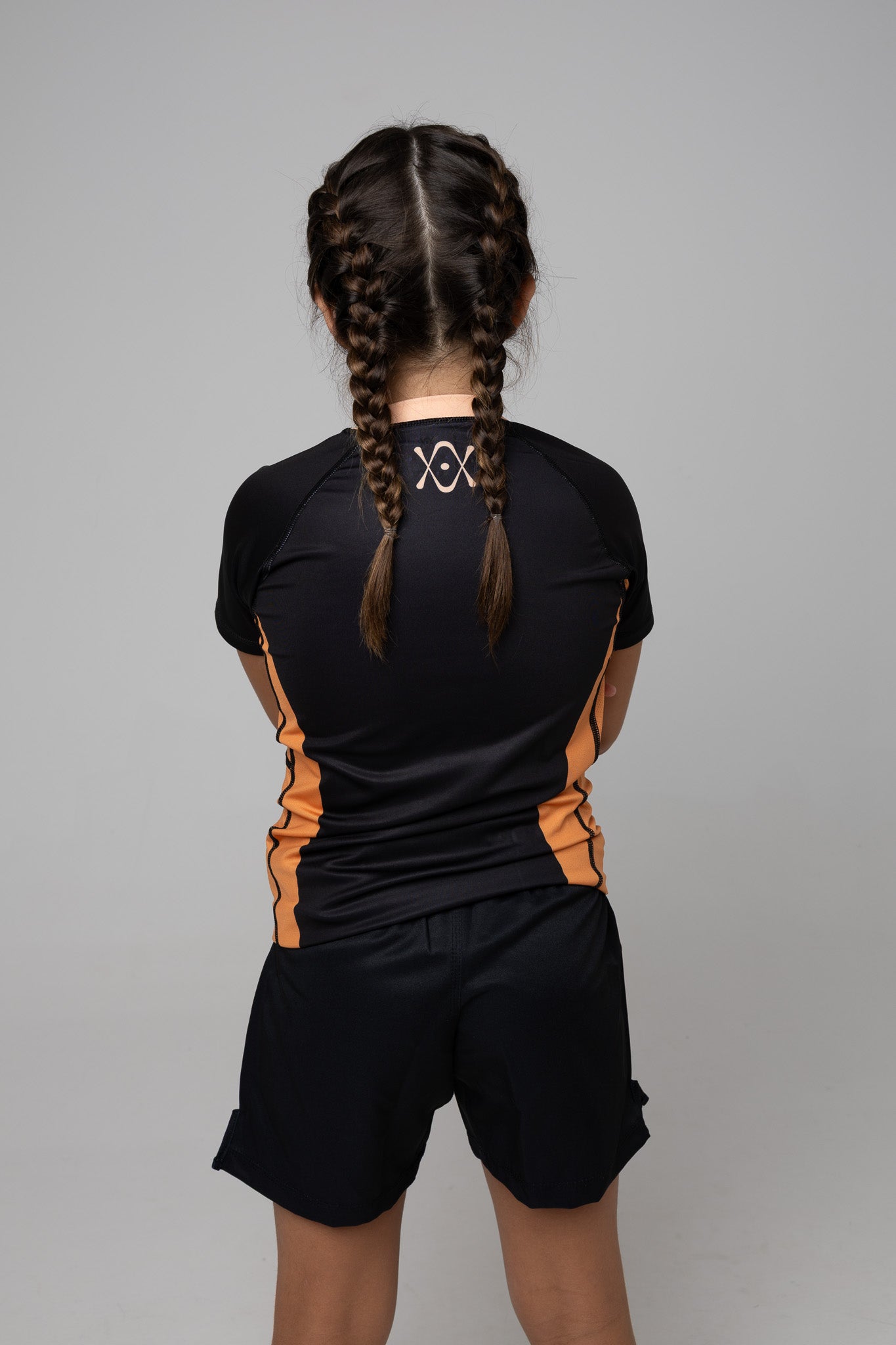 Vista trasera de rashguard negra y naranja AUTŌRITA kids para Brazilian Jiu-Jitsu con logo en la espalda.