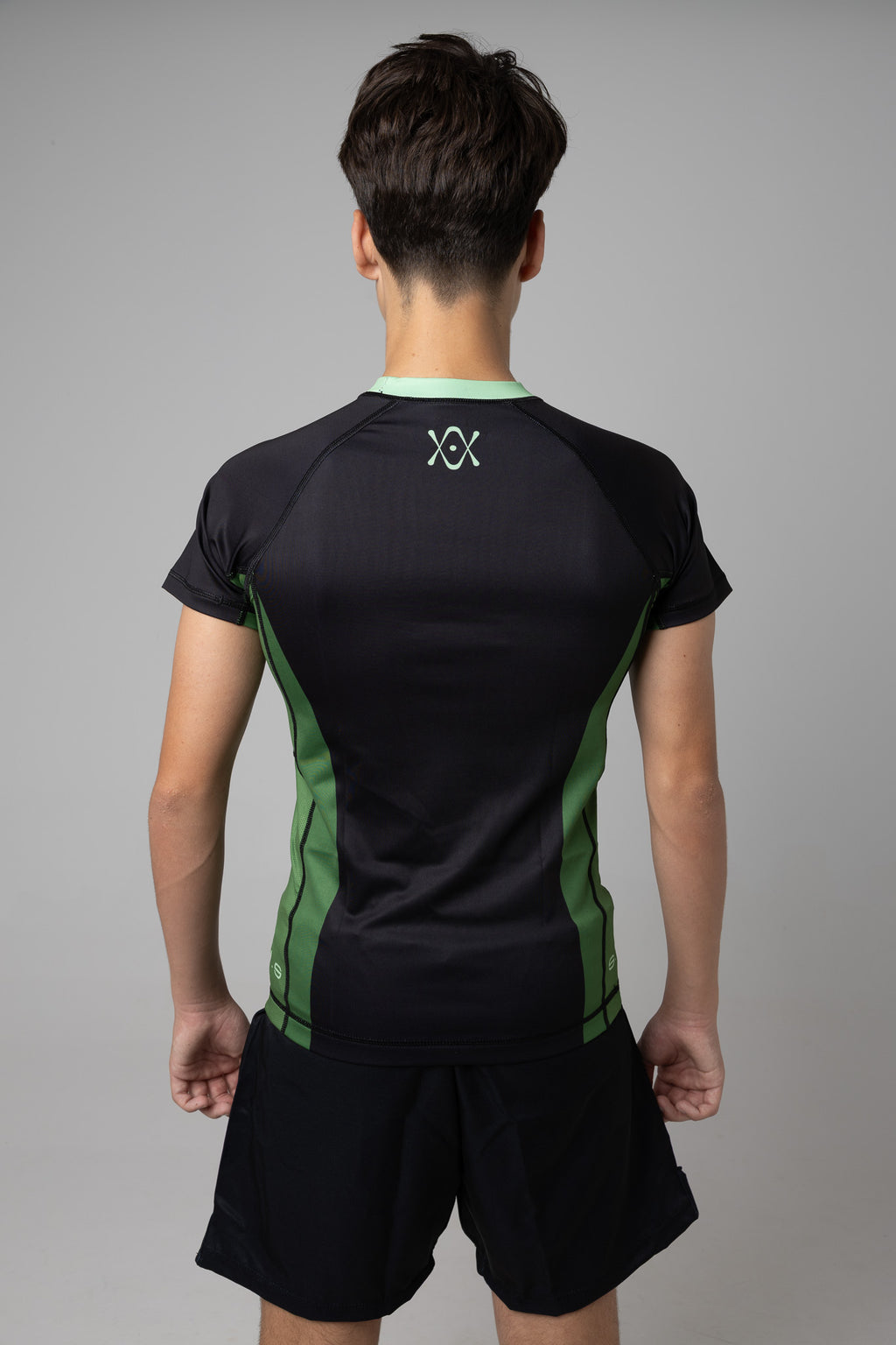 Vista trasera de rashguard negra y verde AUTŌRITA juvenil para BJJ con logo en la espalda.