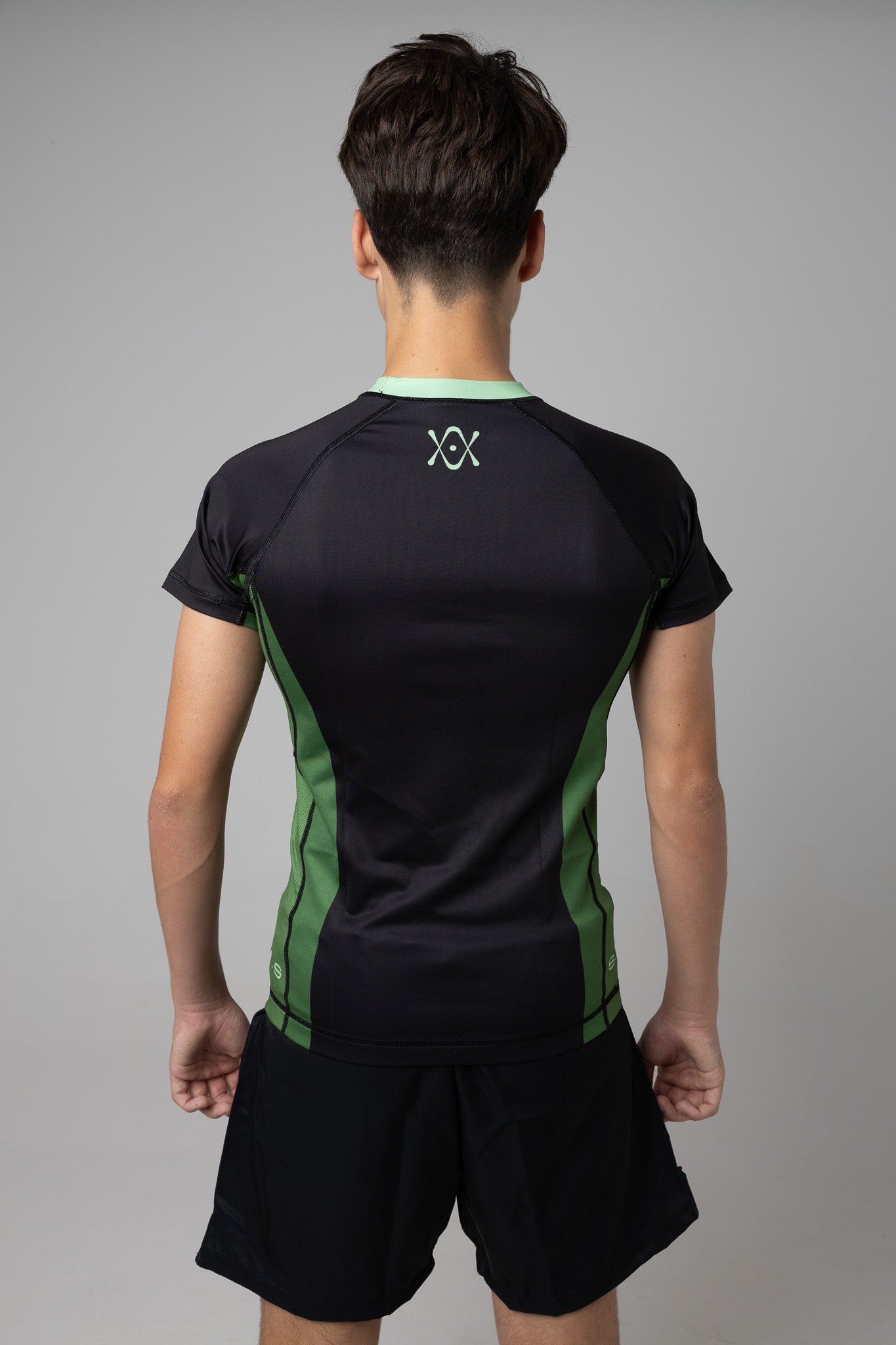 Vista trasera de rashguard negra y verde AUTŌRITA juvenil para BJJ con logo en la espalda.