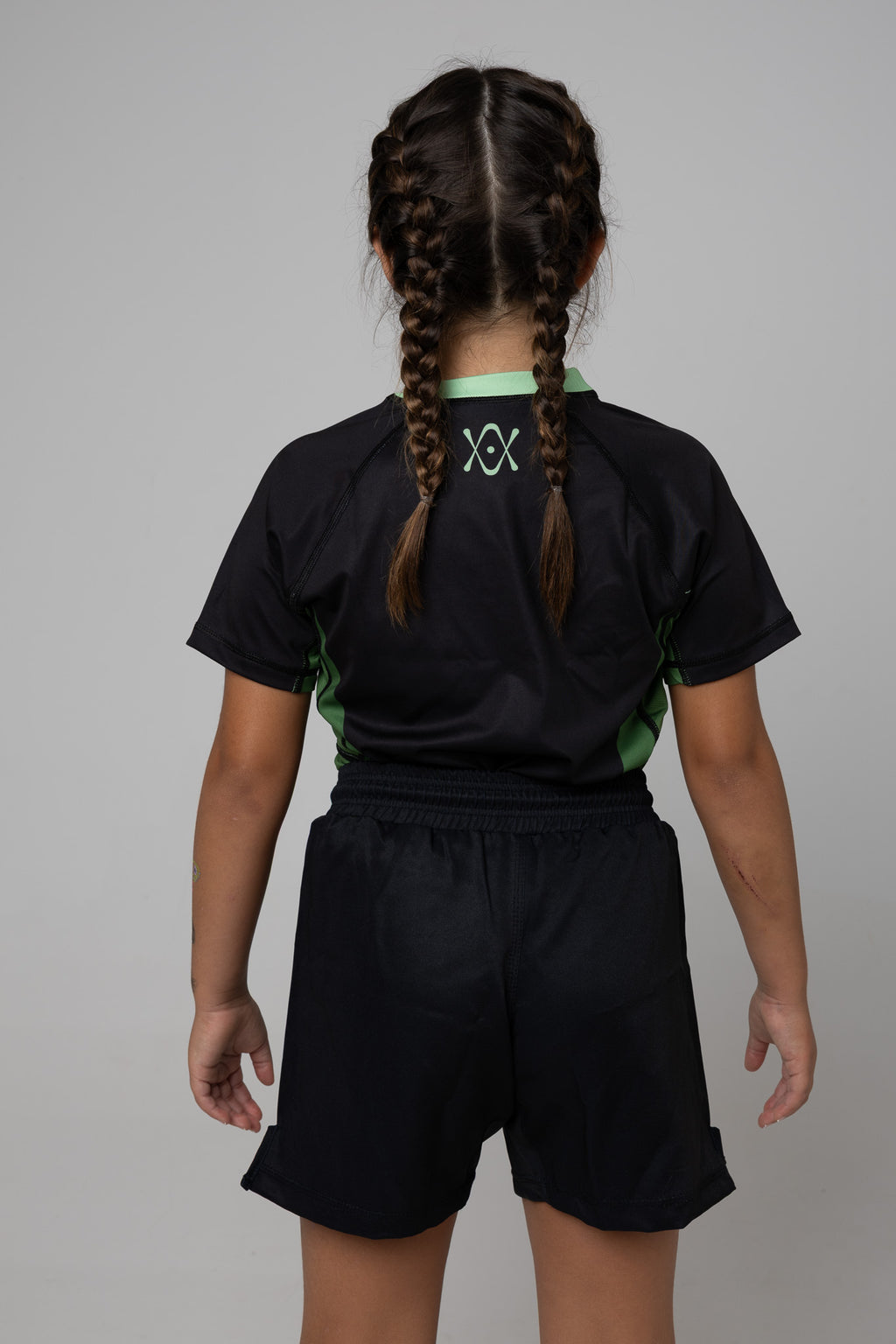 Vista trasera de rashguard negra y verde AUTŌRITA kids para Brazilian Jiu-Jitsu con logo superior.