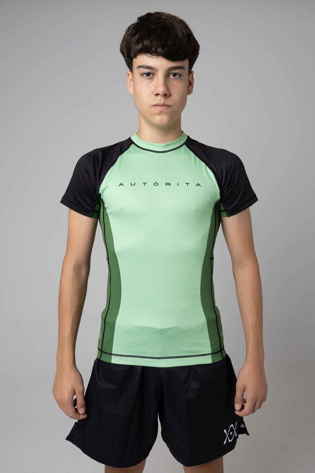 Vista frontal de rashguard verde AUTŌRITA juvenil para Brazilian Jiu-Jitsu y entrenamiento de grappling.