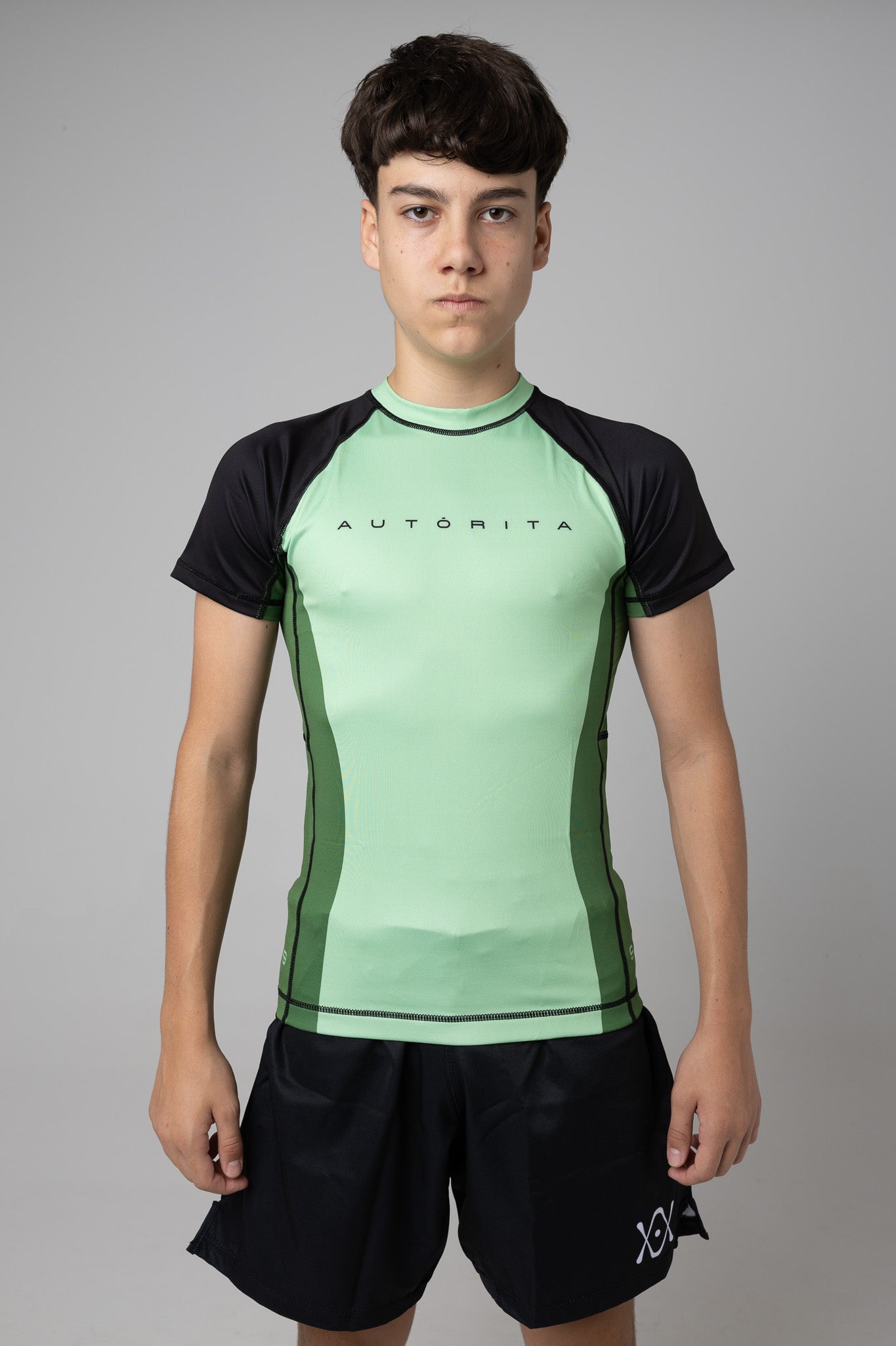 Vista frontal de rashguard verde AUTŌRITA juvenil para Brazilian Jiu-Jitsu y entrenamiento de grappling.
